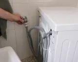 Ręka zakręca zawór wody do pralki, która nie pobiera wody.