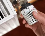 Dłoń reguluje termostat grzejnika, ustawiając go na niską temperaturę. Zimne grzejniki nie grzeją, a oszczędność energii jest priorytetem.