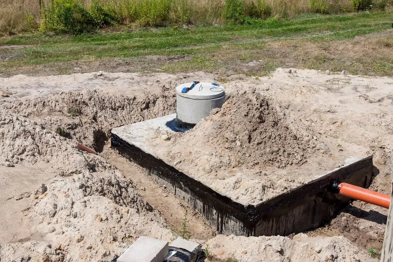 Budowa szamba: betonowa konstrukcja z rurą wylotową, przygotowana do uszczelnienia.