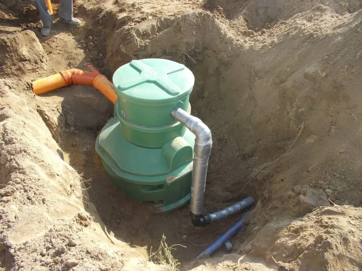 Instalacja kanalizacji ciśnieniowej: zielony zbiornik i pomarańczowe rury w wykopie.