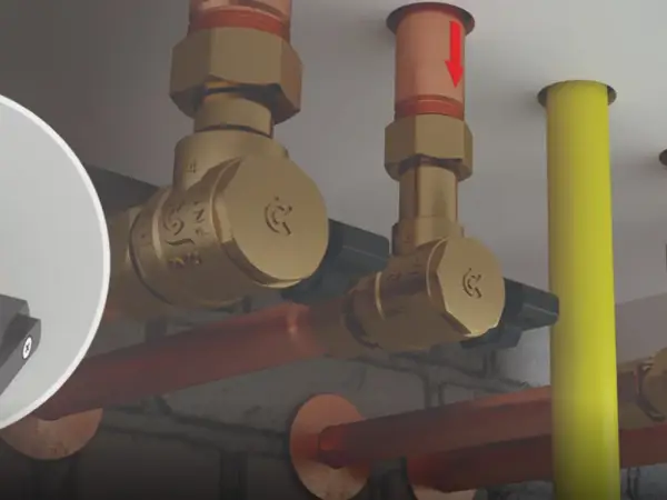 Widok instalacji hydraulicznej z mosiężnymi zaworami. Czerwona strzałka na rurze miedzianej pokazuje, jak działa zawór zwrotny, zapobiegając cofaniu się płynu.