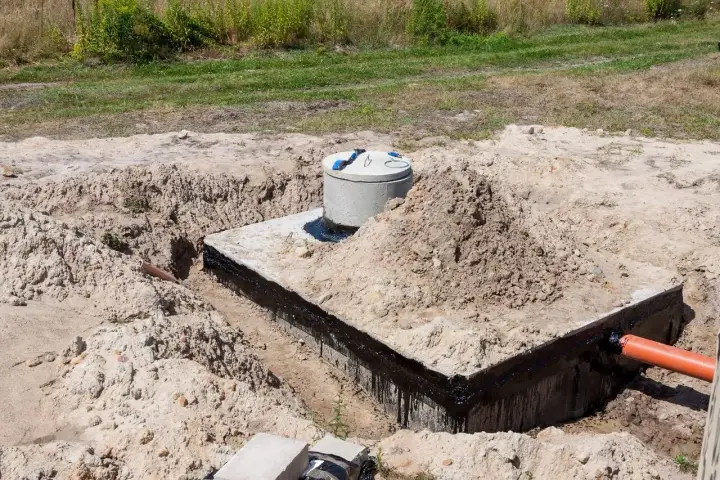 Budowa szamba: betonowa konstrukcja z rurą wylotową, przygotowana do uszczelnienia.
